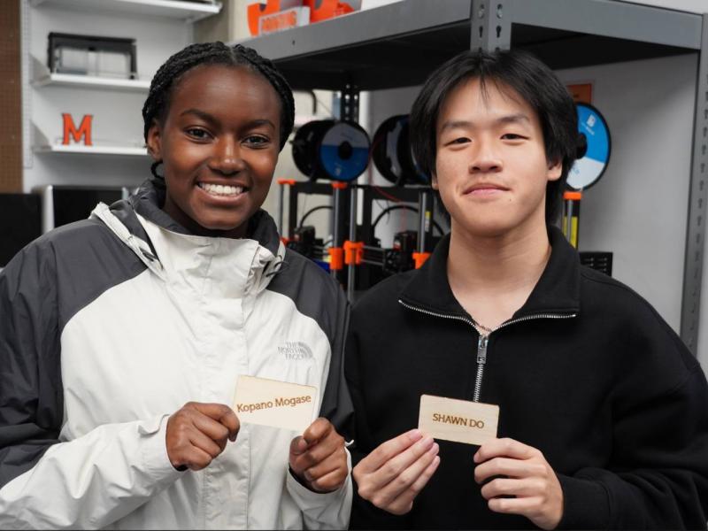 2 Students posing with their custom plywood name tags made in the workshop